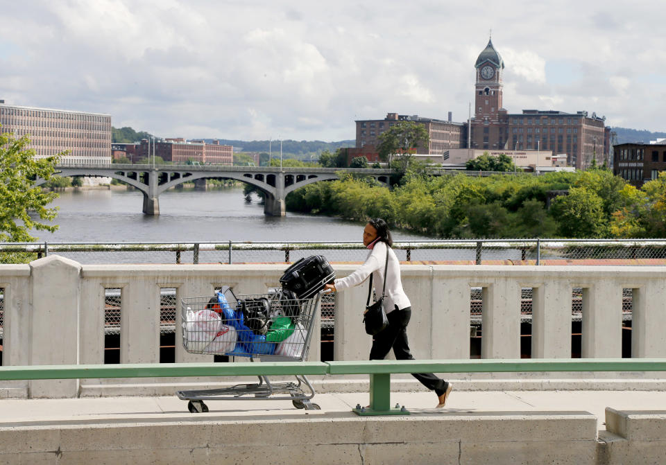 A resident talks on her cell phone as she pushes a grocery cart full of belongings across the Merrimack River on South Broadway in Lawrence, Mass., Friday, Sept. 14, 2018. Multiple houses were damaged Thursday afternoon from gas explosions and fires triggered by a problem with a gas line that feeds homes in several communities north of Boston. (AP Photo/(AP Photo/Mary Schwalm)