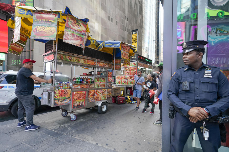 A New York City police officer watches as Youssef Mohamed, left, moves his hot dog cart into his spot on 45th Street in New York's Times Square, Wednesday, Sept. 14, 2022. It's becoming clearer that New York City's recovery from the pandemic will be drawn out and that some aspects of the city's economic ecosystem could be changed for good. More workers returned to their offices as the summer ended. But those limited numbers mean continued hardship for New Yorkers whose jobs are built around the commuting class. (AP Photo/Mary Altaffer)