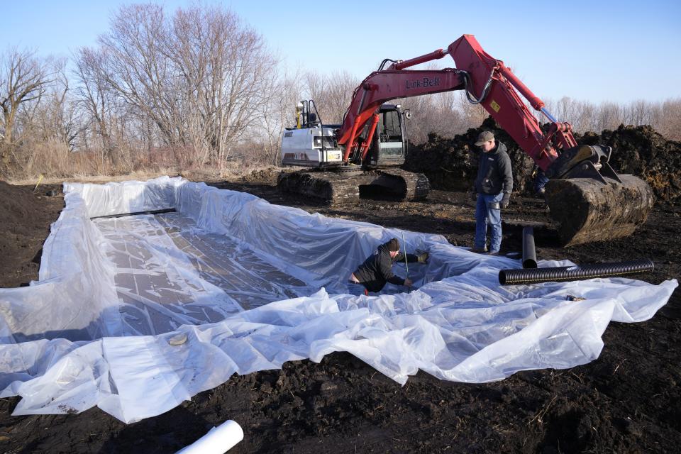 Workers prepare to install wood chips in a bioreactor trench in a farm field, Tuesday, March 28, 2023, near Roland, Iowa. Simple systems called bioreactors and streamside buffers help filter nitrates from rainwater before it can reach streams and rivers. (AP Photo/Charlie Neibergall)