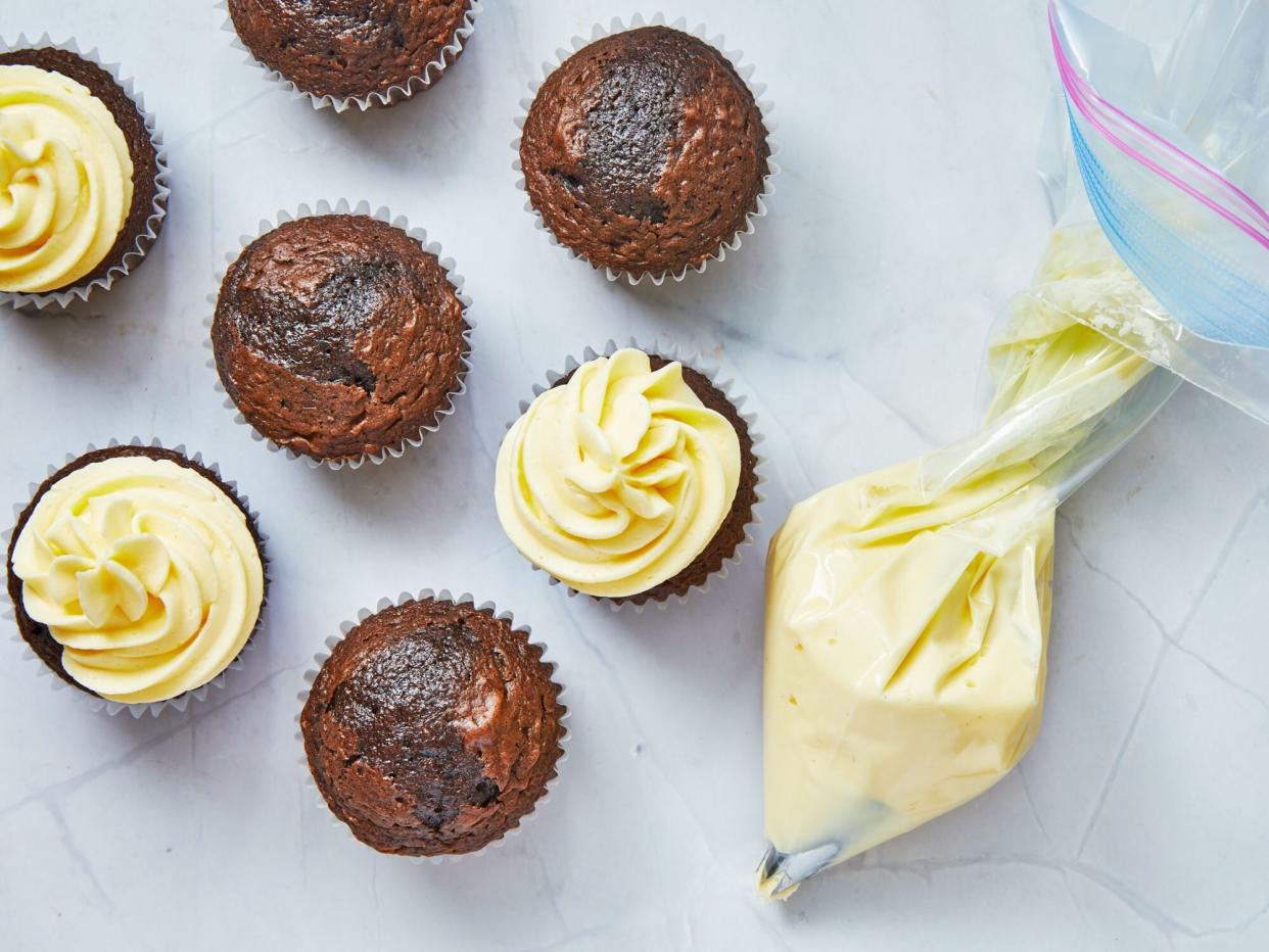 chocolate cupcakes are frosted with a bag of frosting beside them