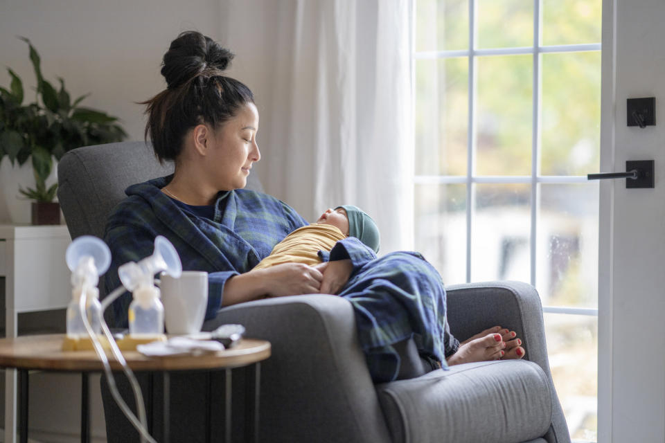 A woman holds her baby as a breast pump sits on a table beside them