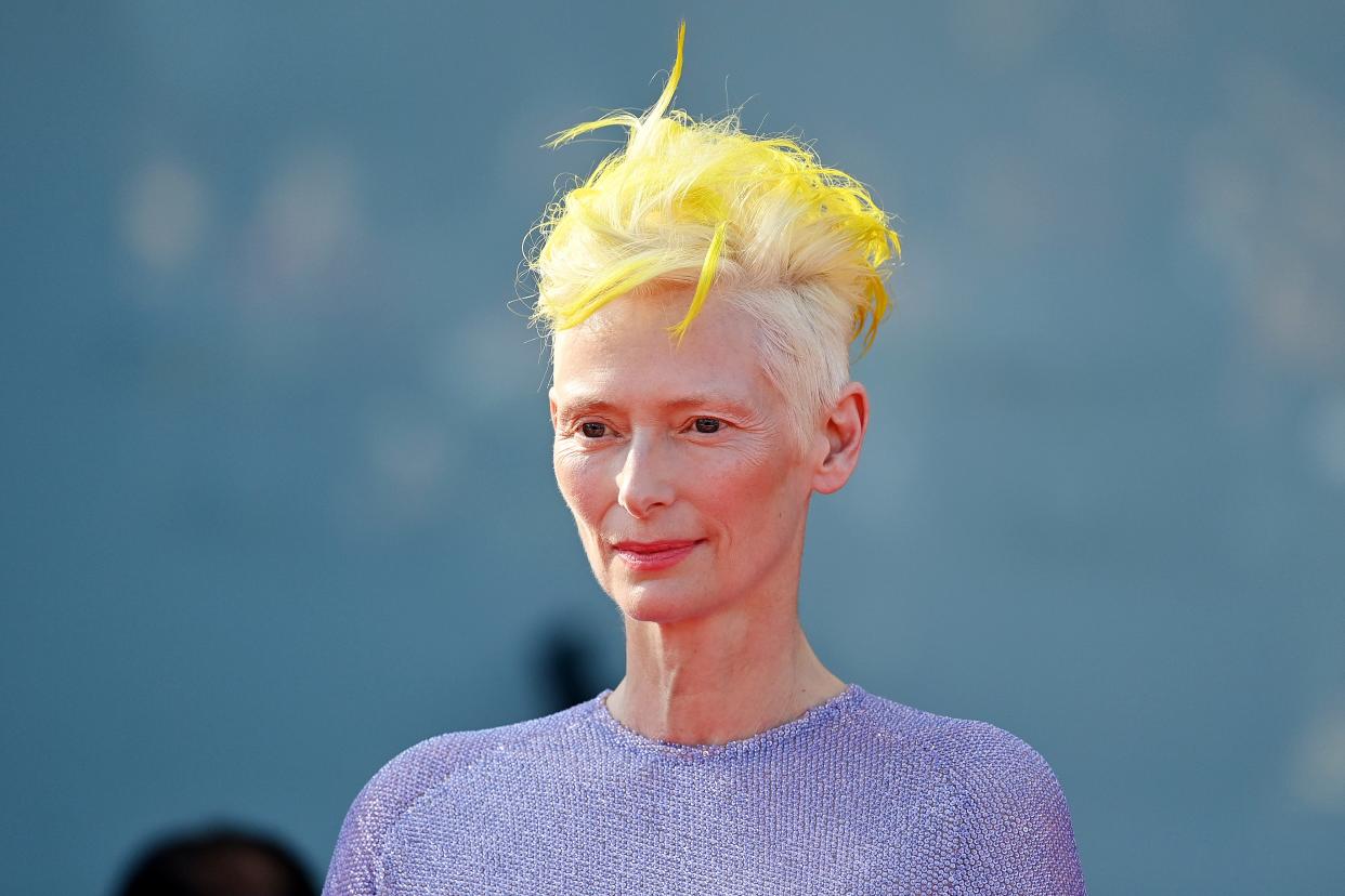 Tilda Swinton with neon yellow hair and a purple dress