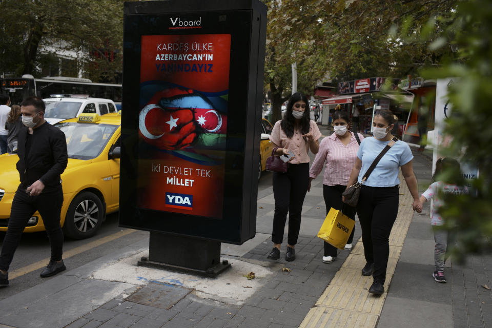 People wearing masks to help protect against the spread of coronavirus, walk past a billboard that reads " Turkey and Azerbaijan, two states one nation " in Ankara, Turkey, Thursday, Oct. 8, 2020. Turkish President Recep Tayyip Erdogan on Thursday again reiterated his country's full support to Azerbaijan, which he said was determined to reclaim its territory.(AP Photo/Burhan Ozbilici)