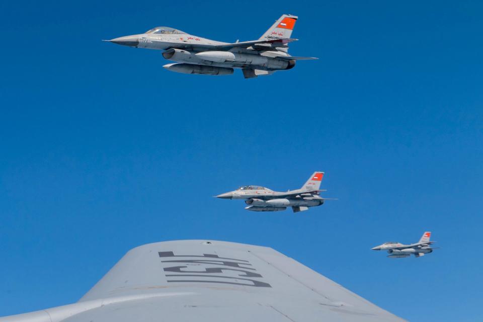 A view from the wing of an aircraft of three F-16 fighter jets against a clear sky.