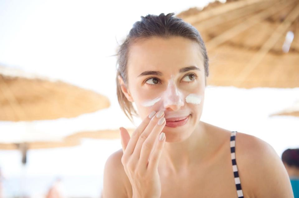 woman smears face sunscreen at the beach for protection