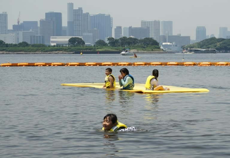Children swim at Odaiba seaside park in Tokyo Bay with the skyline of the world's biggest city shimmering behind them