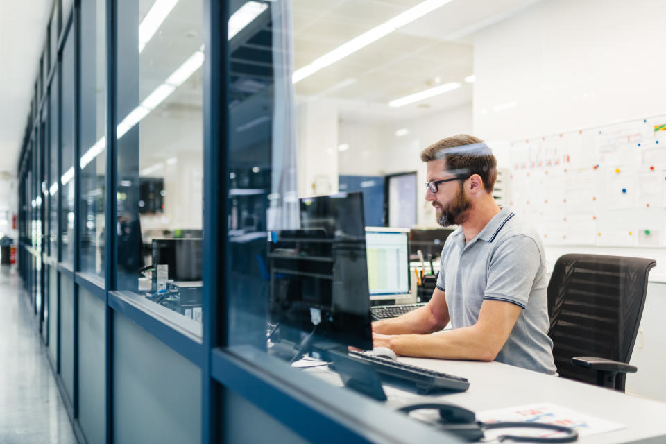 Technician working in control room of a factory looking on computer monitors and tracking production