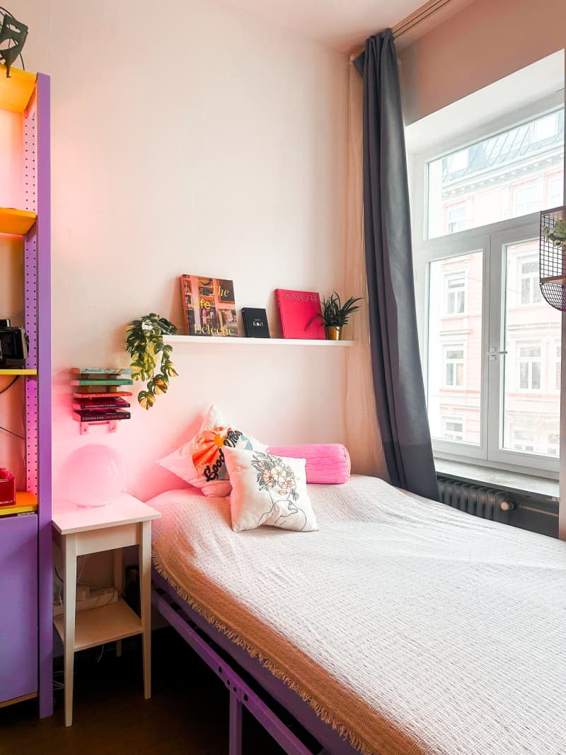 simple bed in corner with pink round lamp and small white wood nightstand