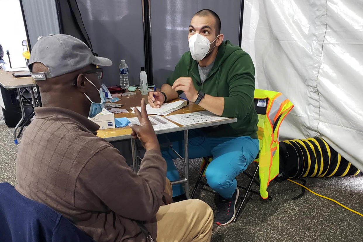 In this March 12, 2021 photo provided by Unity Health Care, Othon Sosua, right, talks with a patient during a vaccination drive in Washington, D.C. Homeless Americans who have been left off priority lists for coronavirus vaccinations — or even bumped aside as states shifted eligibility to older age groups — are finally getting their shots as vaccine supplies increase. Walk-up vaccine events are crucial for a population with limited access to cars, cellphones or Wi-Fi, organizers say. (Unity Health Care via AP)