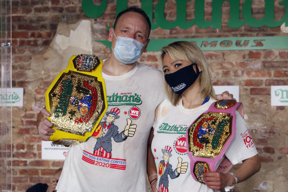 Joey Chestnut, izquierda, y Miki Sudo posan para la cámara tras imponer nuevos récords mundiales y defender sus títulos de campeones _de las divisiones masculina y femenina respectivamente_ del famoso concurso de comer más “perros calientes” que organiza la cadena de restaurantes Nathan’s Famous, el sábado 4 de julio de 2020, en Nueva York. (AP Foto/John Minchillo)