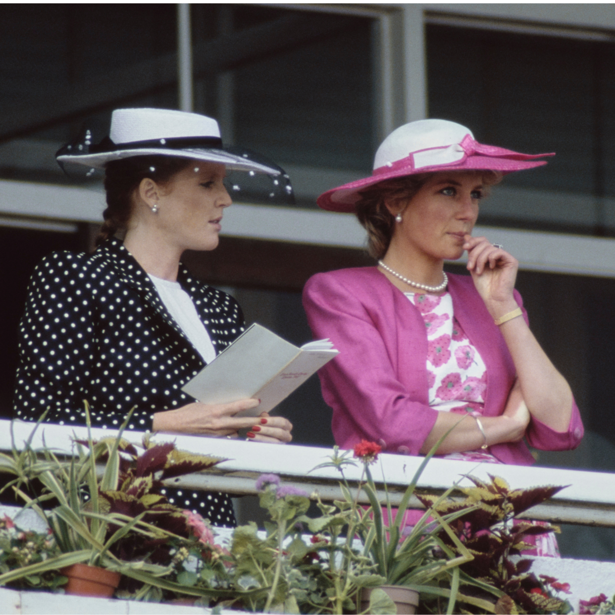  British Royals Sarah, Duchess of York, wearing a dark blue outfit with white polka dots and white wide brim hat with a dark blue band, and Diana, Princess of Wales (1961-1997), wearing a pink Catherine Walker suit with a white silk floral blouse, and a matching pink-and-white hat by Philip Sommerville, attend the Derby Day meeting at Epsom Downs Racecourse in Epsom, Surrey, 3rd June 1987 