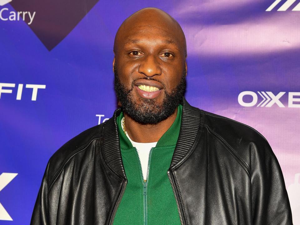 Lamar Odom smiling at OxeFit event in green sweater and leather jacket