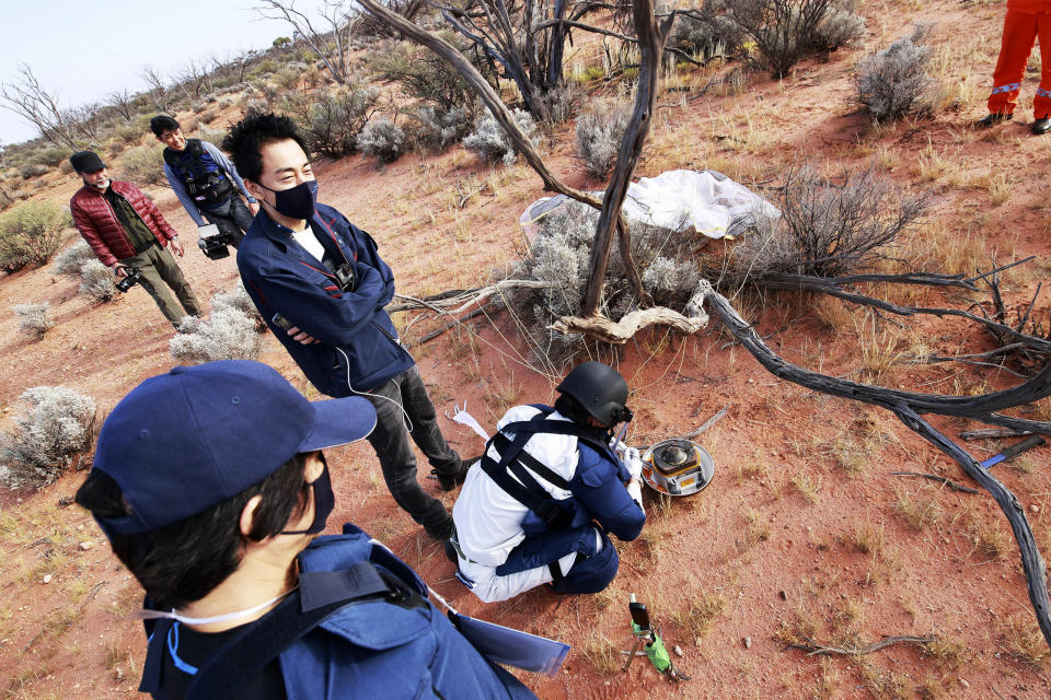 In this photo provided by the Japan Aerospace Exploration Agency (JAXA), members of JAXA retrieve a capsule dropped by Hayabusa2 in Woomera, southern Australia, Sunday, Dec. 6, 2020. A Japanese capsule carrying the first samples of asteroid subsurface shot across the night atmosphere early Sunday before successfully landing in the remote Australian Outback, completing a mission to provide clues to the origin of the solar system and life on Earth. (JAXA via AP)