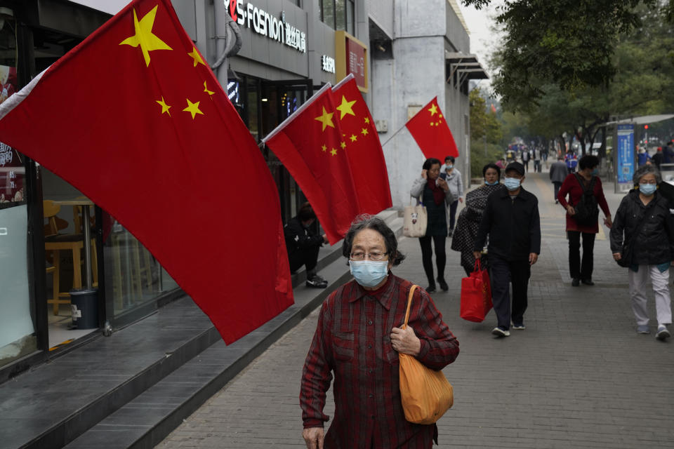 A woman wearing a mask to protect herself from the coronavirus passes by national flags on the last day of the National Day holidays in Beijing on Thursday, Oct. 8, 2020. The eight-day holiday this year, which coincides with the Mid-Autumn Festival, will be a litmus test of whether China's tourism industry can bounce back following the battering it took earlier in the year. (AP Photo/Ng Han Guan)