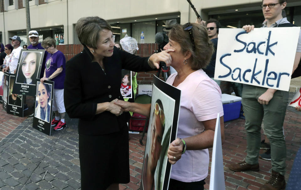FILE - In this Friday, Aug. 2, 2019 file photo, Massachusetts Attorney General Maura Healey, left, wipes a tear from the face of Wendy Werbiskis, of East Hampton, Mass., one of the protesters gathered outside a courthouse in Boston, where a judge was to hear arguments in state's lawsuit against Purdue Pharma over its role in the national drug epidemic. The end of the Purdue Pharma bankruptcy case has left a bitter taste for those who wanted to see more accountability for the Sackler family. They will pay more than $4 billion under the settlement but also will escape any future liability over the nation’s opioid crisis. (AP Photo/Charles Krupa, File)
