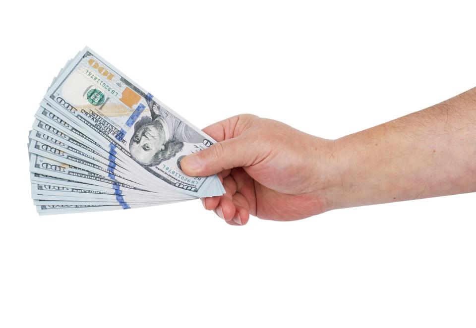 A hand holding a fanned-out stack of US hundred-dollar bills, isolated on a white background