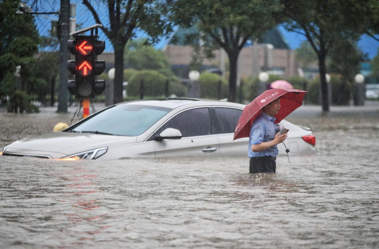 A man wades past a submerged car along a flooded street following heavy rains in Zhengzhou on Tuesday (AFP via Getty Images)