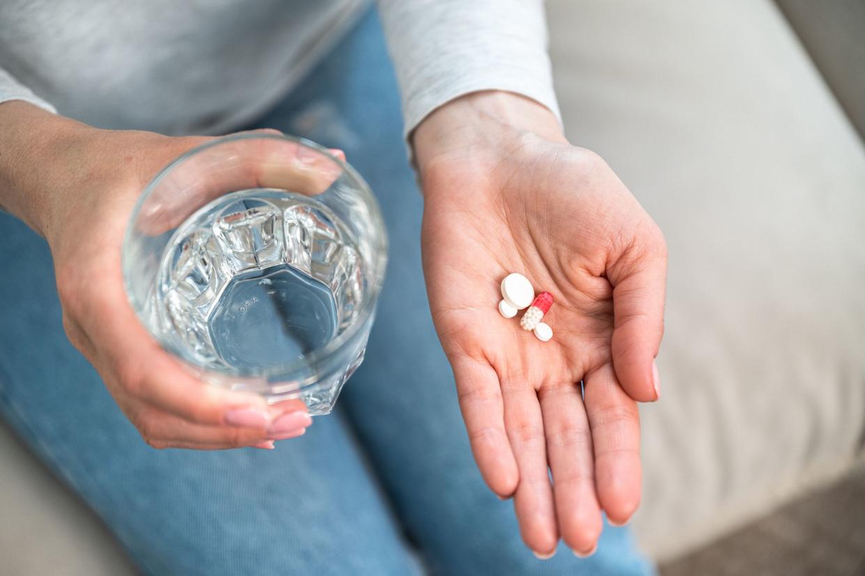 high angle view of female hand hold glass of water and medication pills in palm, taking sedative tablets from anxiety disorder. woman with daily dose of vitamin supplements for healthy life, top view