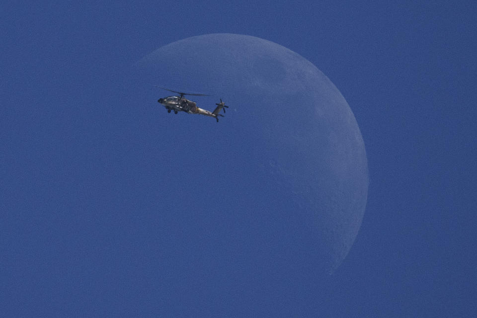 An Israeli helicopter flies over the Israeli-Gaza border, backdropped by the moon, as seen from southern Israel, Thursday, Feb. 15, 2024. (AP Photo/Leo Correa)