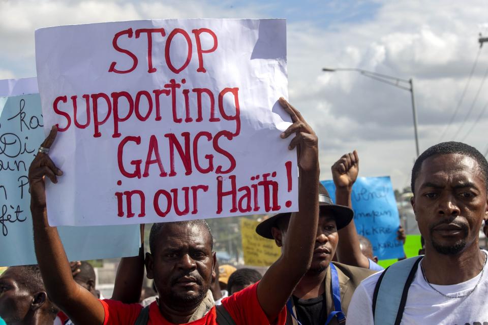 FILE - In this Dec. 10, 2020 file photo, a protester holds a sign with a message to stop supporting gangs during a protest demanding the resignation of Haitian President Jovenel Moise in Port-au-Prince, Haiti. A UNICEF report says that escalating gang violence has displaced thousands of women and children in the capital in the first two weeks of June 2021. (AP Photo/Dieu Nalio Chery, File)