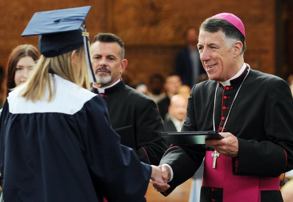With Msgr. Joseph G. Celano, pastor of Immaculate Conception Parish, Somerville, standing nearby, Bishop James F. Checchio confers a diploma on a graduating senior of Immaculata High School during the Friday, June 3, commencement ceremony.