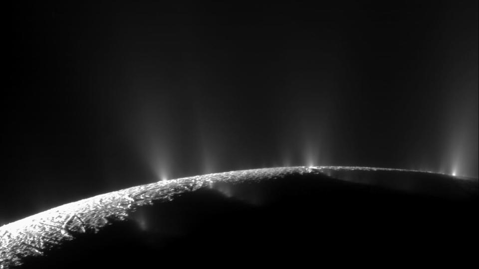 water plumes from the moon enceladus erupting into space. the curve of the moon is visible against the black of space