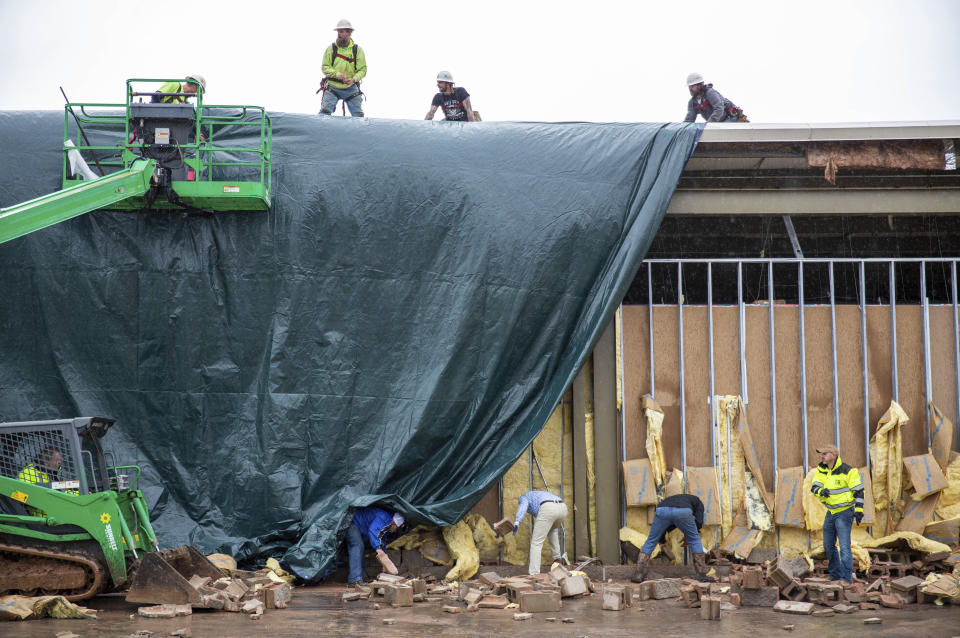 Stewart Richey Electrical employees and other utility workers and city crews help clear debris and put up a large tarp at Thornton Furniture on Cave Mill Road in Bowling Green, Ky., after another tornado warning was issued late Saturday morning, Jan. 1, 2022, for Warren and surrounding counties, following the devastating tornadoes that tore through town on Dec. 11, 2021. Though the damage from Saturday's storm proved less catastrophic than the system that passed through in December, heavy rain and strong winds battered the area, causing damage along Cave Mill Road and the surrounding area. (Grace Ramey/Daily News via AP)