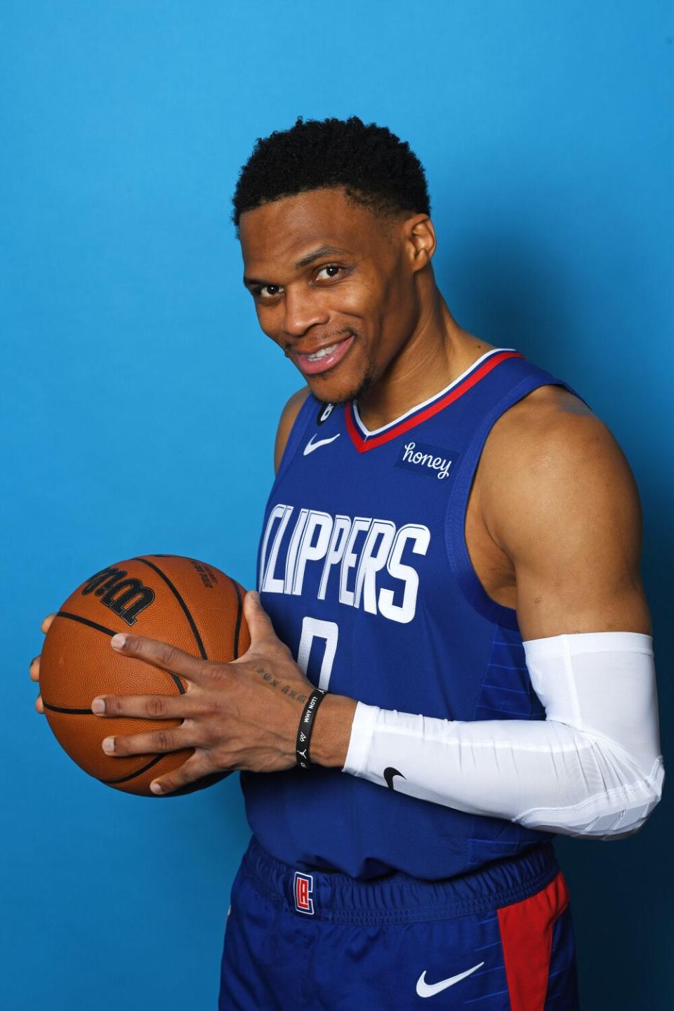 Russell Westbrook smiles and holds a basketball in a portrait.