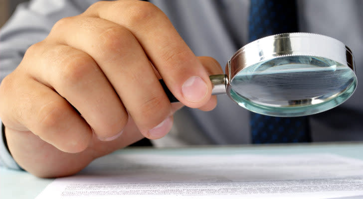 A photo of a hand holding a magnifying glass and looking at a paper.