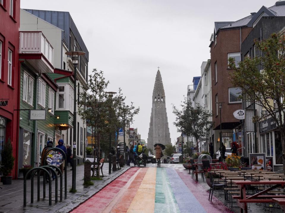 A rainbow-painted road in Iceland with a view of a church tower in the distance