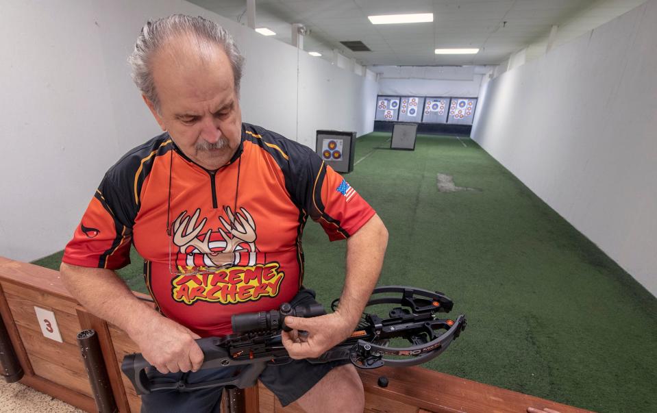 Bill Reider, co-owner of Xtreme Archery, works on a crossbow in front of an archery shooting range carpeted in recycled artificial turf from a former college football field.