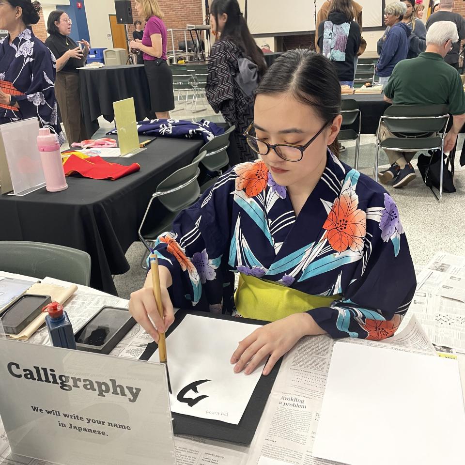 Manami Kishimoto, clad in a yukata, writes a student's name in Japanese calligraphy.