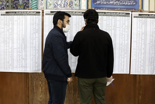 Voters wearing face masks check the list of the candidates in the parliamentary elections in a polling station in Tehran, Iran