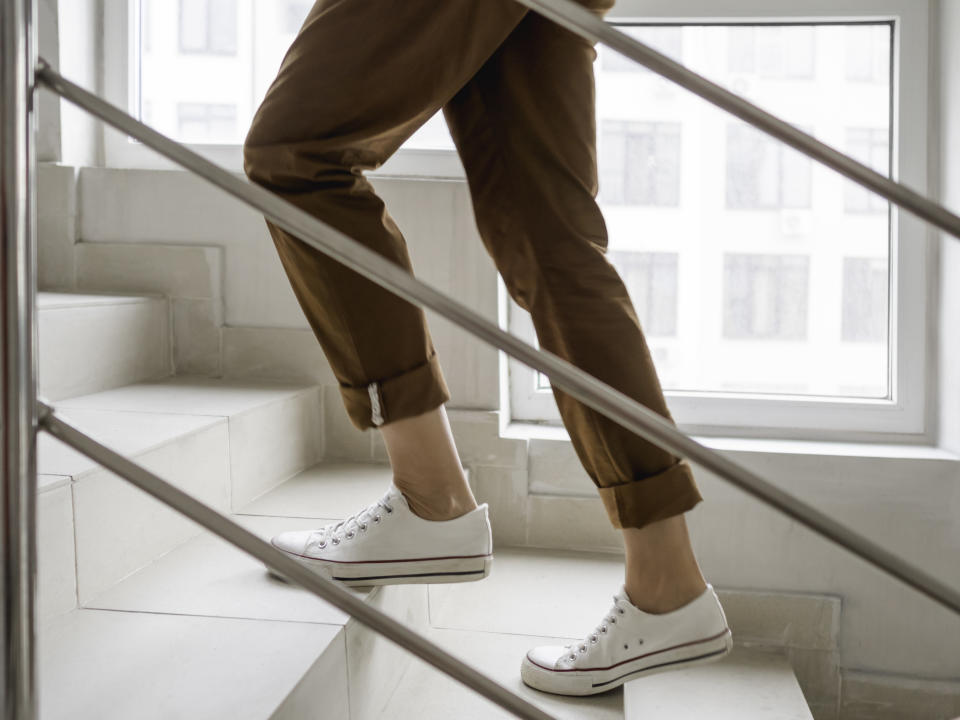 Woman in white sneakers and khaki trousers goes upstairs to her apartment. White staircase in apartment building. Casual outfit, urban fashion.