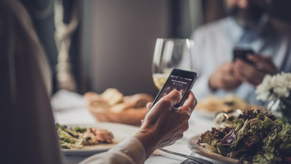 Close up of unrecognizable mature woman entering a PIN on her cell phone while being in a restaurant with her husband.