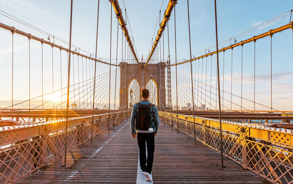 Rear view of a young man walking on the Brooklyn Bridge at sunrise. (Alexander Spatari / Getty Images)