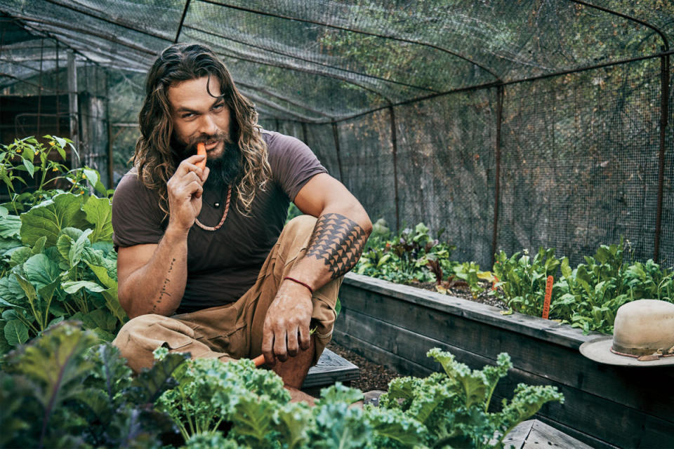 Jason Momoa eating a carrot in his home greenhouse, where he grows squash, eggplants, carrots, basil, kale, arugula, and collard greens.<p>Jeff Lipsky for Men's Journal</p>