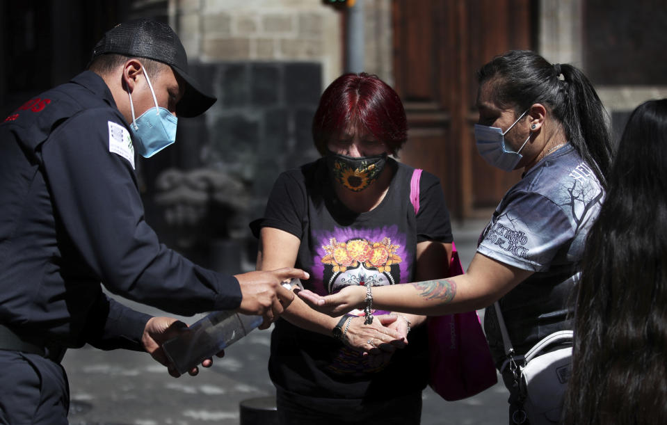 A firefighter gives disinfectant gel to women out shopping after authorities changed the health alert to orange after weeks in red, in Mexico City, Saturday, Feb. 13. 2021, amid the new coronavirus pandemic. (AP Photo/Marco Ugarte)