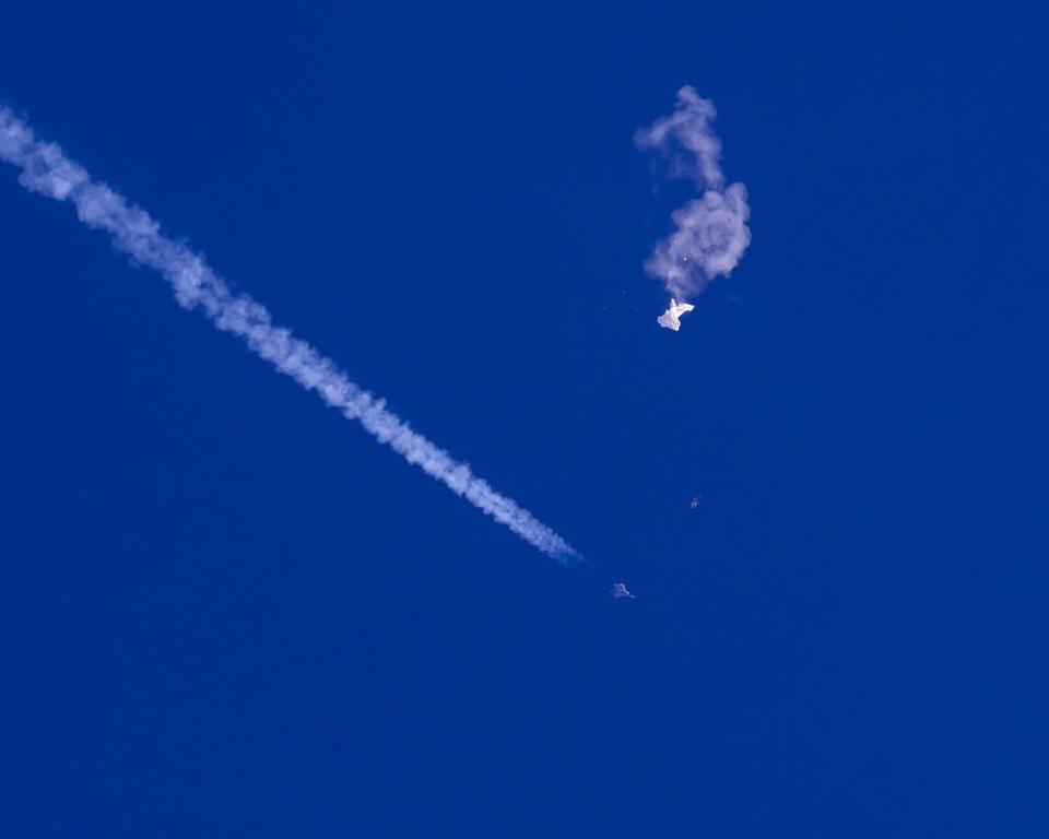 In this photo provided by Chad Fish, the remnants of a large balloon drift above the Atlantic Ocean, just off the coast of South Carolina, with a fighter jet and its contrail seen below it, Saturday, Feb. 4, 2023. The downing of the suspected Chinese spy balloon by a missile from an F-22 fighter jet created a spectacle over one of the state’s tourism hubs and drew crowds reacting with a mixture of bewildered gazing, distress and cheering.