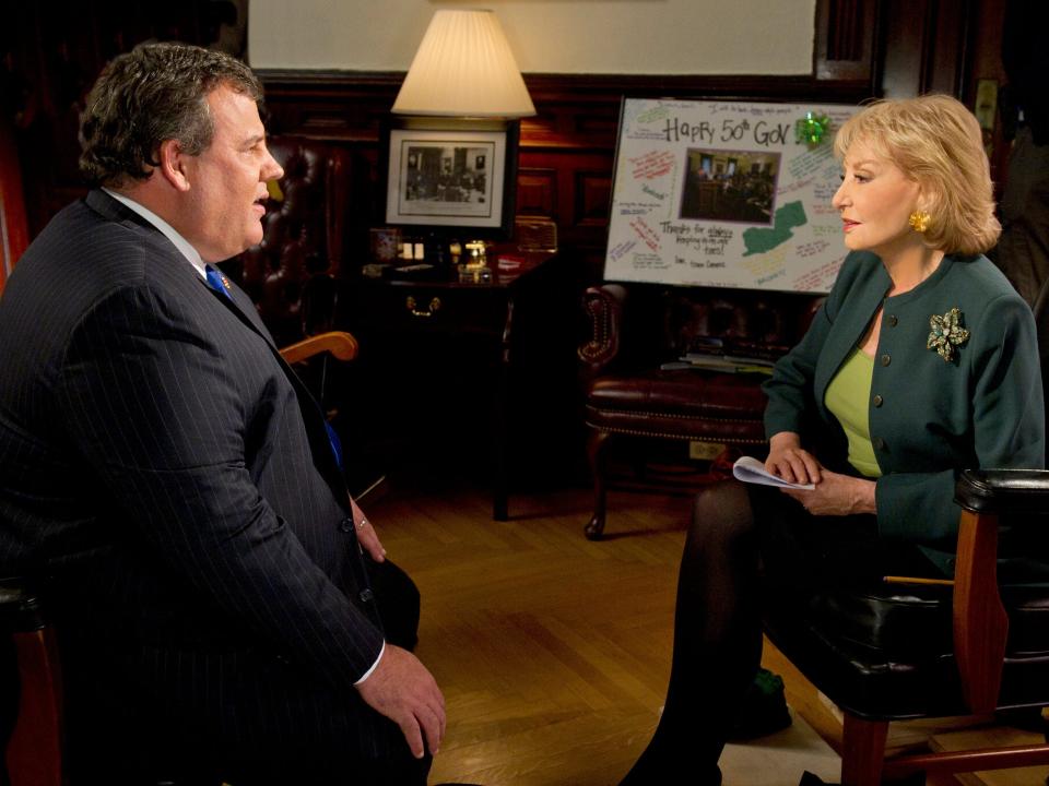 A man with a black suit sits across from a woman in a green jacket