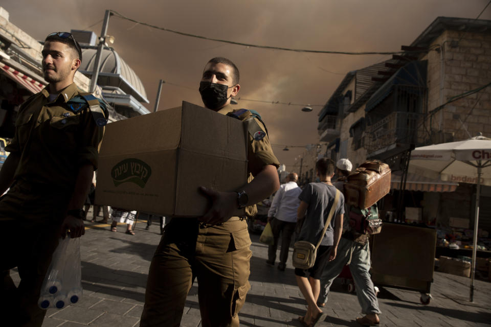 An Israeli soldier carries a box of sandwiches as he walks with a fellow soldier through the Machane Yehuda market under a sky darkened by nearby wildfires, in Jerusalem, Sunday, Aug. 15, 2021.(AP Photo/Maya Alleruzzo)