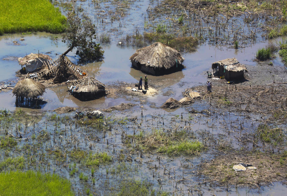 FILE - In this Tuesday March 26, 2019 file photo, a family stand outside their submerged huts near Beira, Mozambique. Beira's mayor Davis Simango dreamed about protecting his people from climate change with much of the city being below sea level on a coastline that experts call one of the world's most vulnerable to global warming's rising waters. (AP Photo/Tsvangirayi Mukwazhi, File)