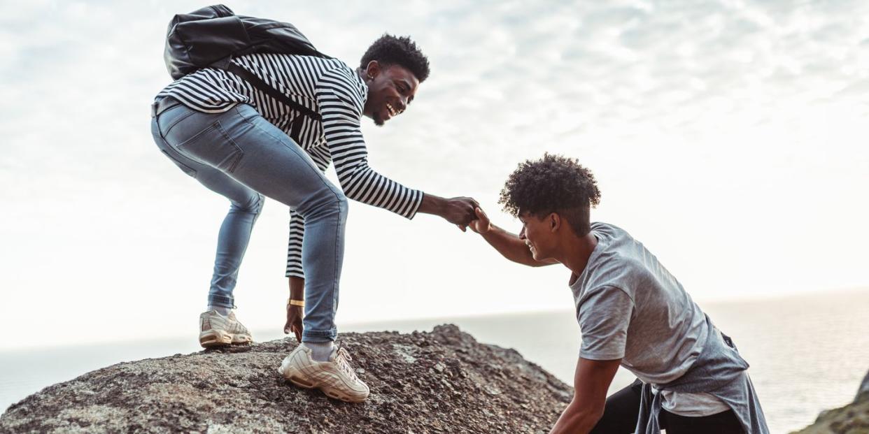 young man helping his friend to climb the rock