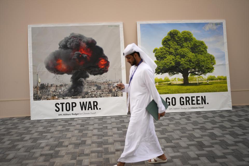 A person walks past signs that read "stop war" and "go green" at the COP28 U.N. Climate Summit, Friday, Dec. 8, 2023, in Dubai, United Arab Emirates. (AP Photo/Rafiq Maqbool)