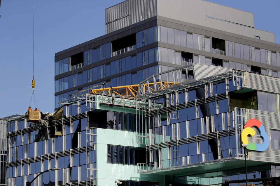 With a portion of the broken crane on the roof behind, workers suspended in a basket survey the damage left on the building when the crane atop it collapsed a day earlier, Sunday, April 28, 2019, in Seattle. The construction crane fell from a building on Google's new campus during a storm that brought wind gusts, crashing down onto one of the city's busiest streets and killing multiple people. (AP Photo/Elaine Thompson)