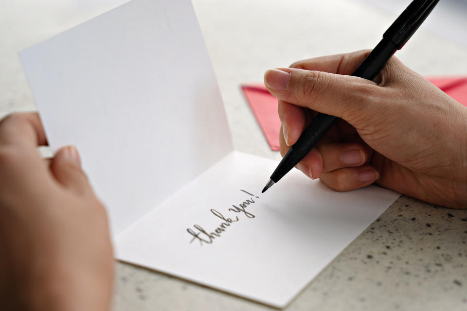 A person is writing "thank you!" on a card