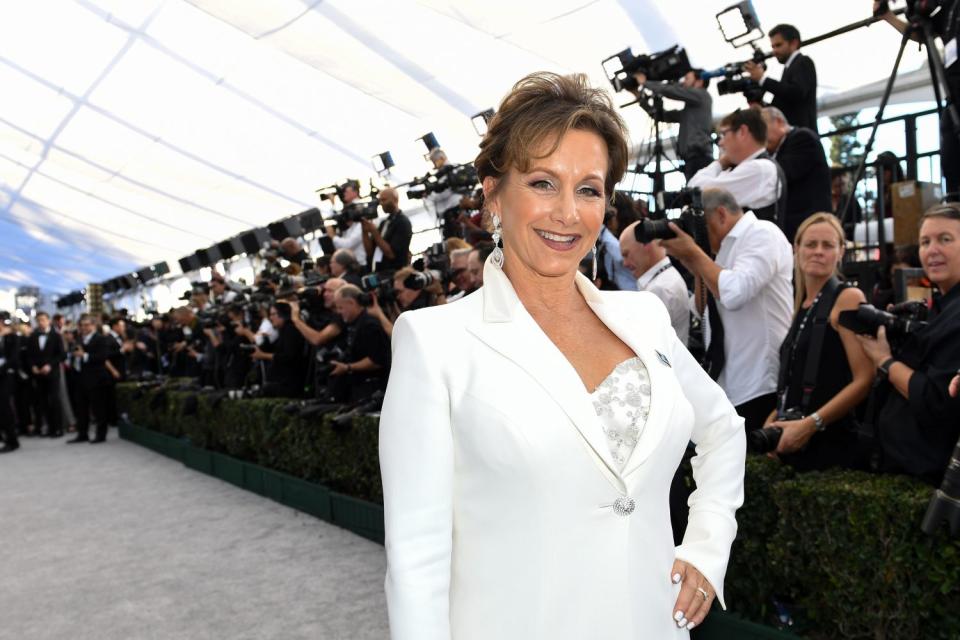 A woman in a white blazer poses on a gray carpet