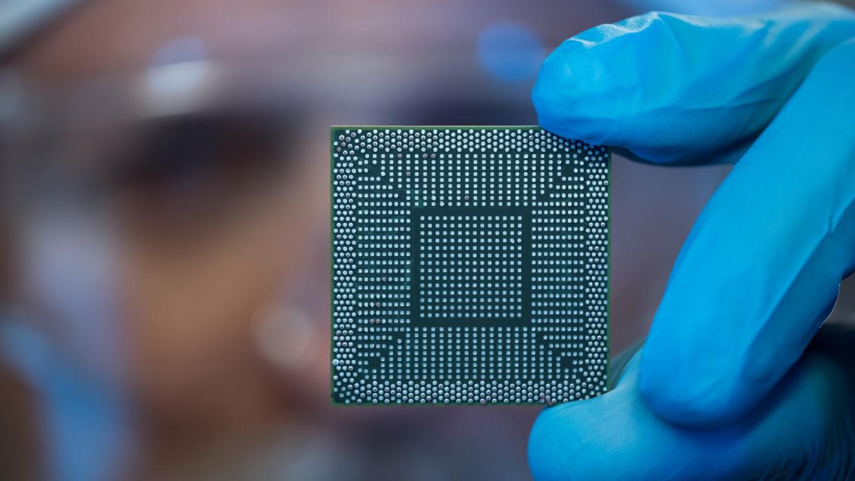 An engineer holds up a microchip to look at it.