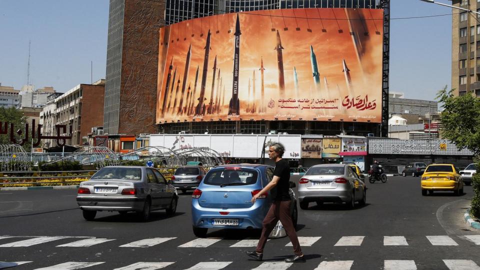 PHOTO: A man crosses a street as motorists drive past a billboard depicting Iranian ballistic missiles in service in Tehran, Apr. 19, 2024.  (AFP via Getty Images)