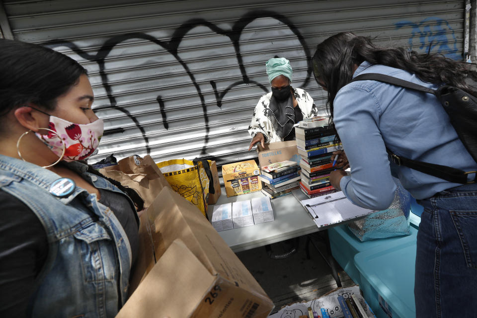 Sistas Van organizer and driver Denise Rodriguez, left, sets up a table with supplies for those in need in front of a shuttered sporting goods store with help from volunteer Shaquaña Williams-Hechavarria, center, and Black Women's Blueprint intern Shabieko Ivy during the current coronavirus outbreak, Tuesday, May 19, 2020, in New York. Launched by Black Women's Blueprint to help survivors of sexual and reproductive violence and physical abuse, the women's network has pivoted during the coronavirus to delivering badly-needed resources to black and Hispanic communities that have been disproportionately affected by the fast-spreading virus. (AP Photo/Kathy Willens)